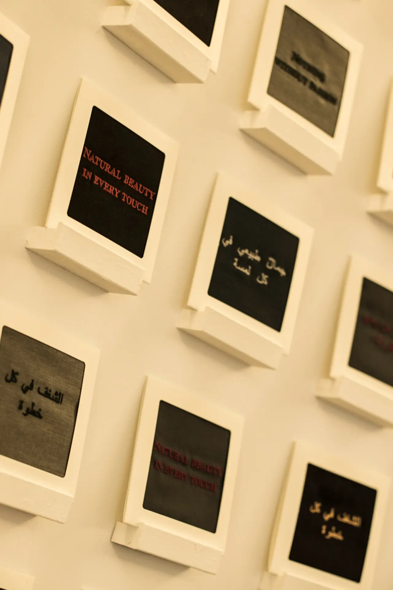 A wall installation of small framed text pieces arranged in a grid, displaying short phrases in multiple languages.